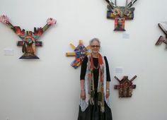 an older woman standing in front of some art on the wall with her hands behind her back