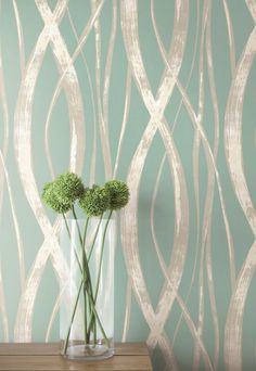 two green flowers in a vase on a table next to a wallpapered background