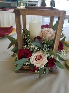 an arrangement of roses and greenery in a wooden frame on a table with candles