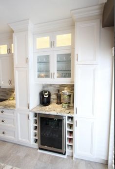 a kitchen with white cabinets and marble counter tops, including a wine cooler in the center