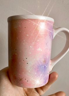 a hand holding a pink and purple coffee mug with stars on the inside, in front of a white wall