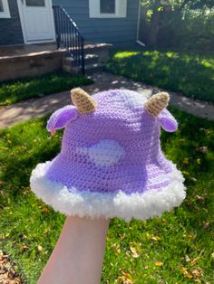 a hand wearing a purple and white crocheted hat with two horns on it