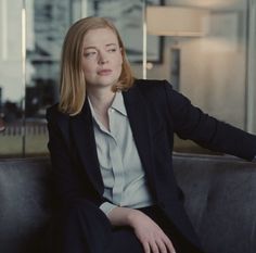 a woman sitting on top of a couch in front of a glass wall and lamp