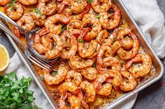 a pan filled with cooked shrimp and garnished with parsley next to lemon wedges