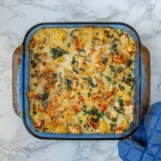 a casserole dish with spinach, cheese and other toppings on a marble surface