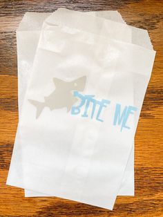 two white bags sitting on top of a wooden table next to each other with bite me stickers on them