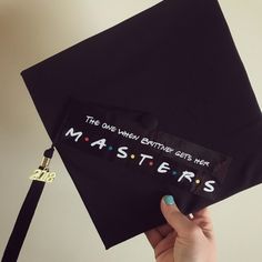 a person holding up a black graduation cap with the words masters on it and a keychain