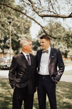 two men in suits standing next to each other under a large tree on the grass