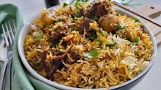 a white bowl filled with rice and meat on top of a green napkin next to a fork