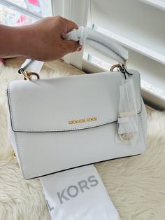 NWT MICHAEL KORS AVA MEDIUM TOP HANDLE SATCHEL Crossbody Bag OPTIC White/Gold Made of Saffiano leather with top handle; Flap with Magnetic inside closure; Back open pocket with snap closure; 1 inside zip pocket; 1 inside open pocket; leather handles of 4 Inches drop; Adjustable and detachable leather shoulder strap of 18-22 Inches drop; Gold tone hardware; Measurements: Length: 11 x Height: 8.5 x Width: 4 Inches; Comes with original tags and dust bag Michael Kors White Bag, Janet Guzman, Dream Lifestyle, Leather Handles, White Bag, Small Tops, Leather Handle, Snap Closure, Top Handle