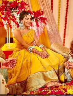 two women in yellow dresses sitting next to each other on a stage with flowers and garlands