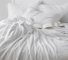 an unmade bed with white sheets and coffee cup on the bottom right corner, in front of it