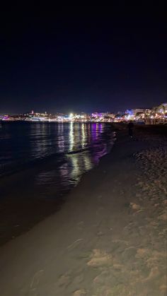 the beach at night is lit up with bright lights and people walking on the sand