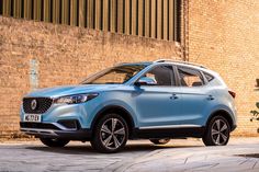 a blue suv is parked in front of a brick wall and shrubbery on the sidewalk