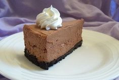 a piece of chocolate cheesecake on a white plate with whipped cream and blue cloth