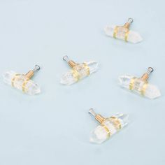 four small clear and gold colored ear plugs on a light blue surface with two yellow pins sticking out of them