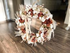 a white wreath with flowers and feathers on a wooden floor in front of a mirror