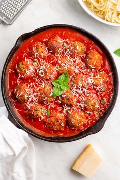 a pan filled with meatballs covered in sauce and parmesan cheese on the side