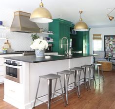 a kitchen with green cabinets and gold pendant lights over the island in front of an oven