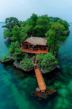 an island with a house on it in the middle of the ocean, surrounded by trees