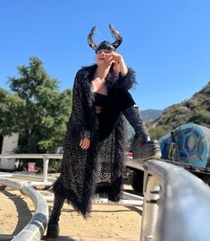 a woman dressed in black with horns on her head is sitting on a metal rail