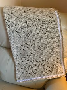 a white crocheted blanket sitting on top of a leather couch next to a pillow