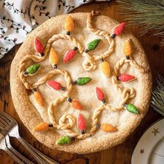 a cookie decorated with fruit and leaves on a wooden table next to silverware, forks and napkins