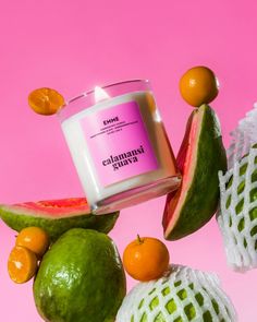 a candle surrounded by fruit on a pink background with oranges and guacamole