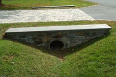 a stone bench sitting in the middle of a grass covered field next to a road