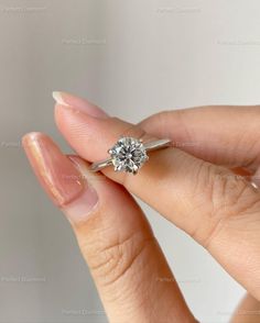 a woman's hand holding an engagement ring with a diamond in the middle, on top of her finger