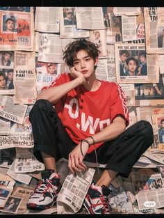 a young man sitting on top of a pile of newspapers with his hand under his chin