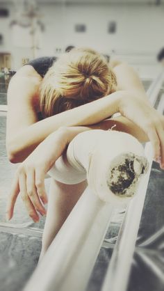 a woman leaning on a metal rail with her arms wrapped around her head and looking down at the ground