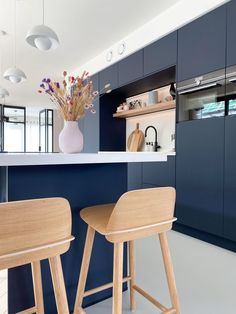 two wooden stools sit in front of a kitchen counter with blue cabinets and shelves