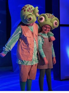 two children dressed in costumes standing next to each other on a blue stage with lights behind them