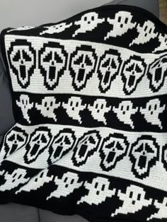 a black and white afghan with skulls on it sitting on a couch next to a pillow