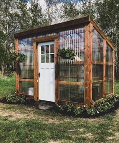 a small wooden structure with a white door and window in the middle of grass field