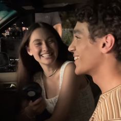 a young man and woman sitting in the back seat of a car smiling at each other