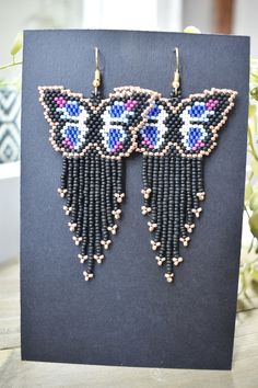 a pair of beaded earrings on top of a black card next to a potted plant