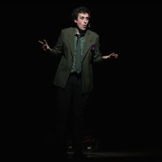 a man in a suit and tie standing on stage with his hands out to the side