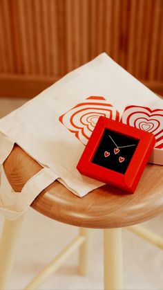 a small red box sitting on top of a wooden table next to a white bag