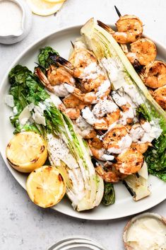 a white plate topped with grilled shrimp and lettuce next to lemon wedges