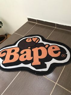 a sign that says bape on the floor in front of a tiled wall with a potted plant next to it