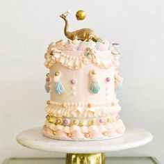 there is a white cake with pink frosting and gold decorations on the top tier