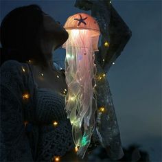 a woman standing in front of a jellyfish lamp with lights on it's sides