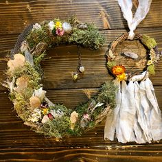 a wreath with flowers and feathers hanging on a wooden wall next to a white scarf