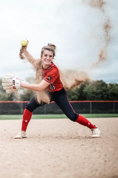 a softball player throwing a ball on top of a field with dirt in the air