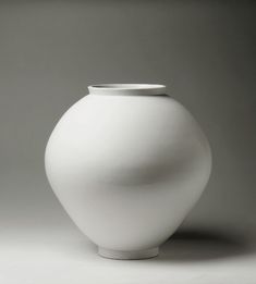 a white vase sitting on top of a gray floor next to a wall in the background