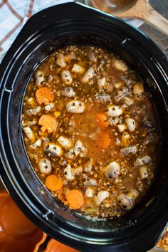 a black crock pot filled with soup and carrots on top of a table