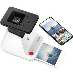 the polaroid camera is next to an open photo album and cell phone on a white surface