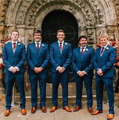 a group of men standing next to each other in front of a stone building wearing suits and ties